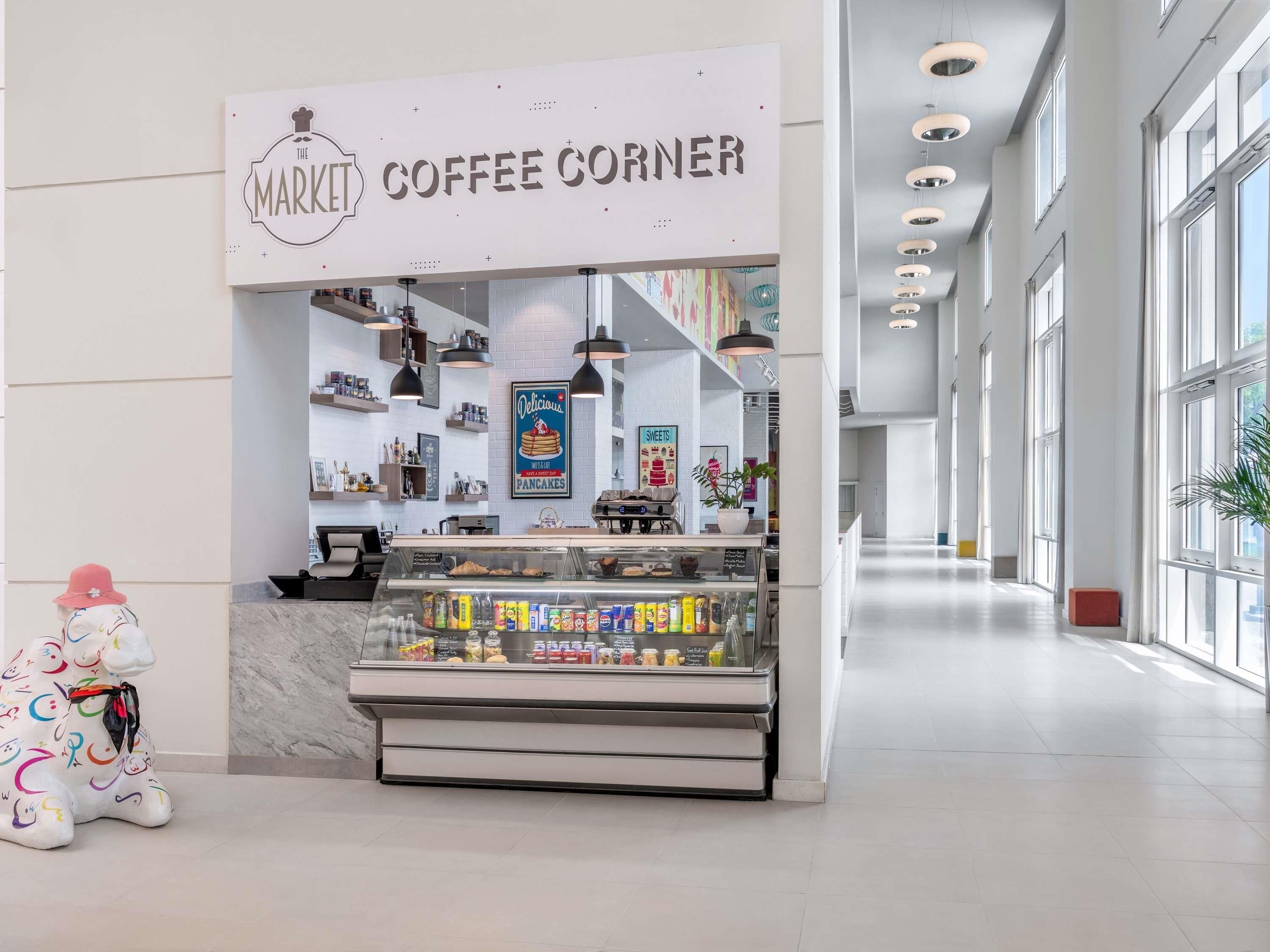 A coffee corner kiosk with a sign reading "The Market Coffee Corner," shelves stocked with various coffee products, and a decorative elephant statue.