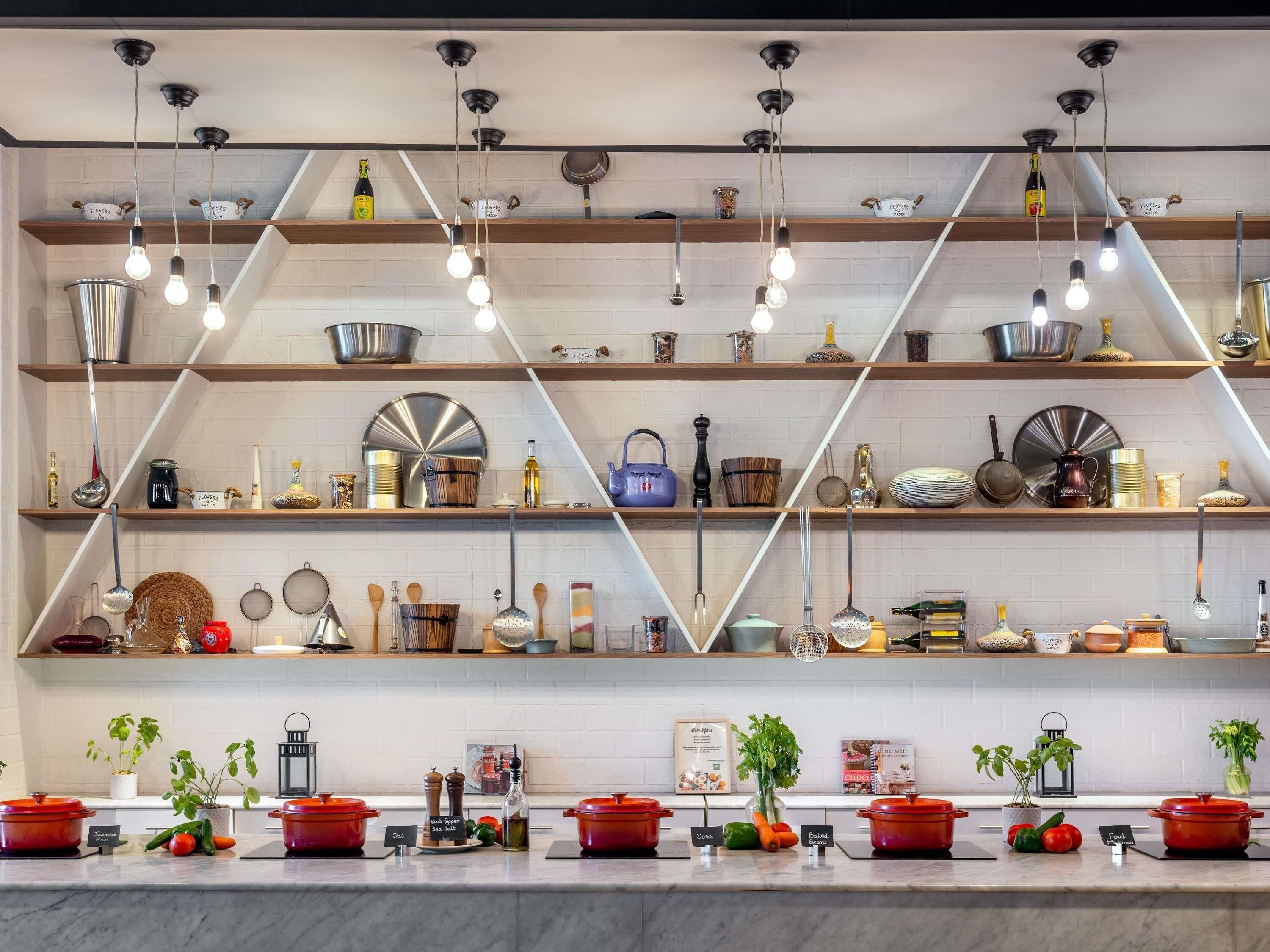 Een keuken met meerdere planken waarop keukengerei staat, een marmeren aanrecht met kookpannen, en hangende lampen.