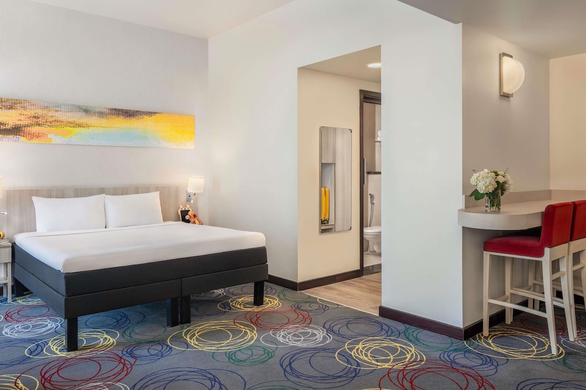Ein Hotelzimmer mit Bett, Schreibtisch und einem durchgegangenen Tür sichtbaren Badezimmer.