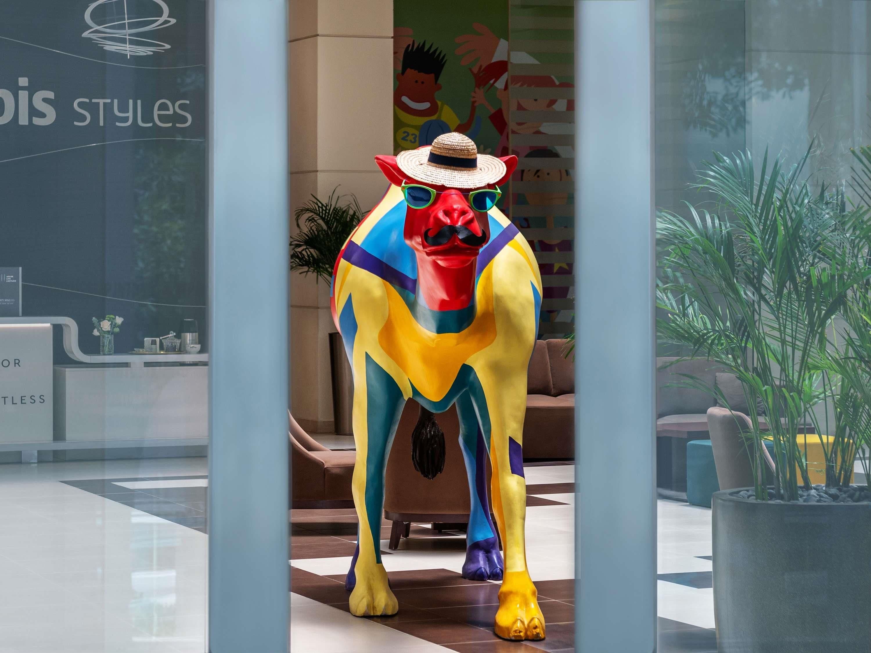 A colorful horse statue in a modern lobby with a glass wall, a reception desk, and potted plants.