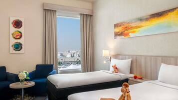A hotel room with two beds, a sofa, a small table with a vase of flowers, and a city view.