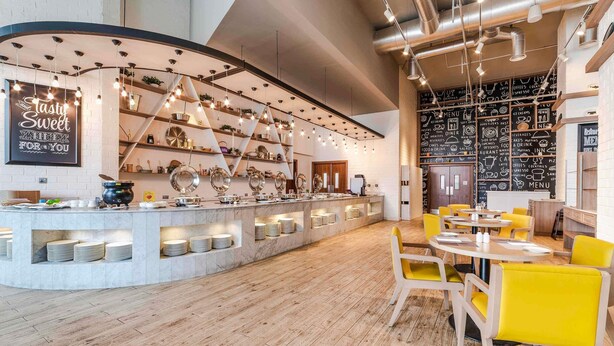 Un interno di un caffè moderno con un bancone centrale, sedie gialle e una lavagna con il menu.