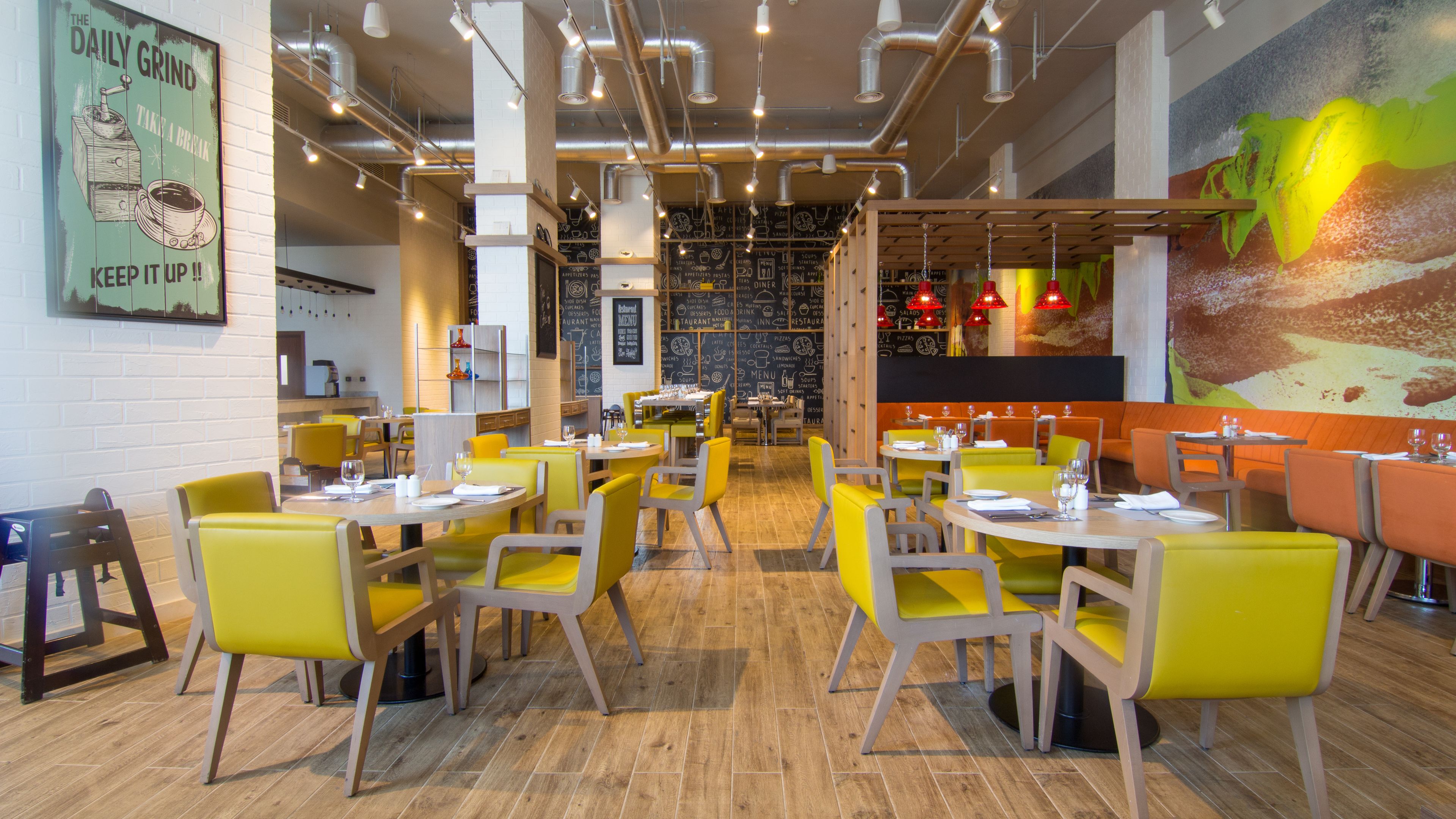 L’intérieur d’un restaurant avec des chaises jaunes, des tables en bois et une fresque murale.