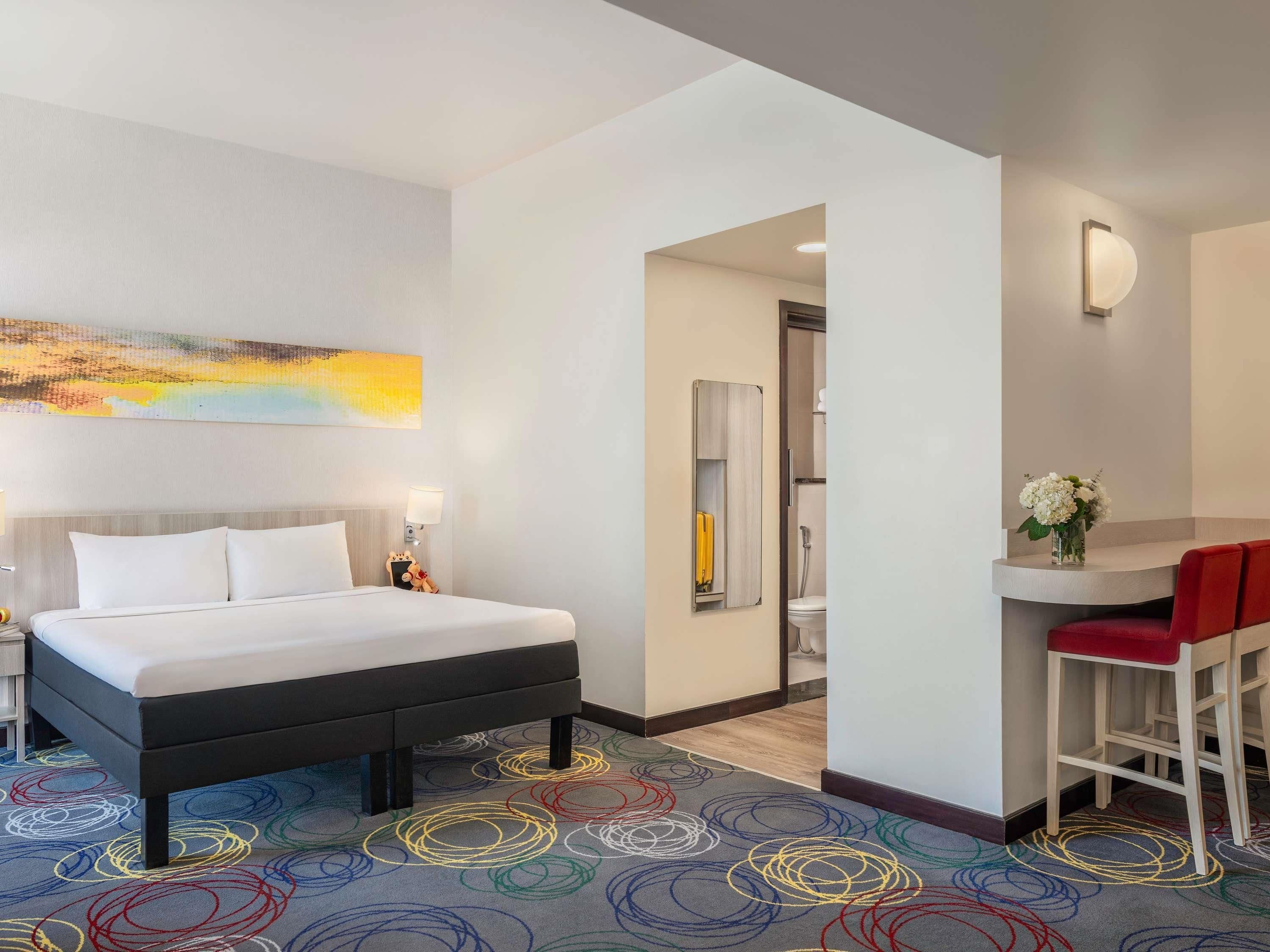 A hotel room with a bed, a desk, and a bathroom visible through an open door.