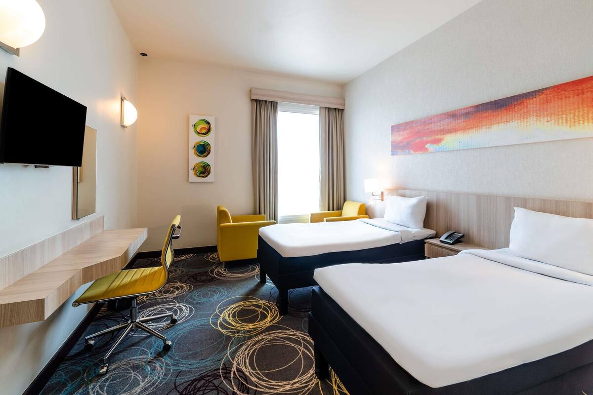 Een hotelkamer met twee bedden, een televisie, een bureau met stoel en een raam met gordijnen.