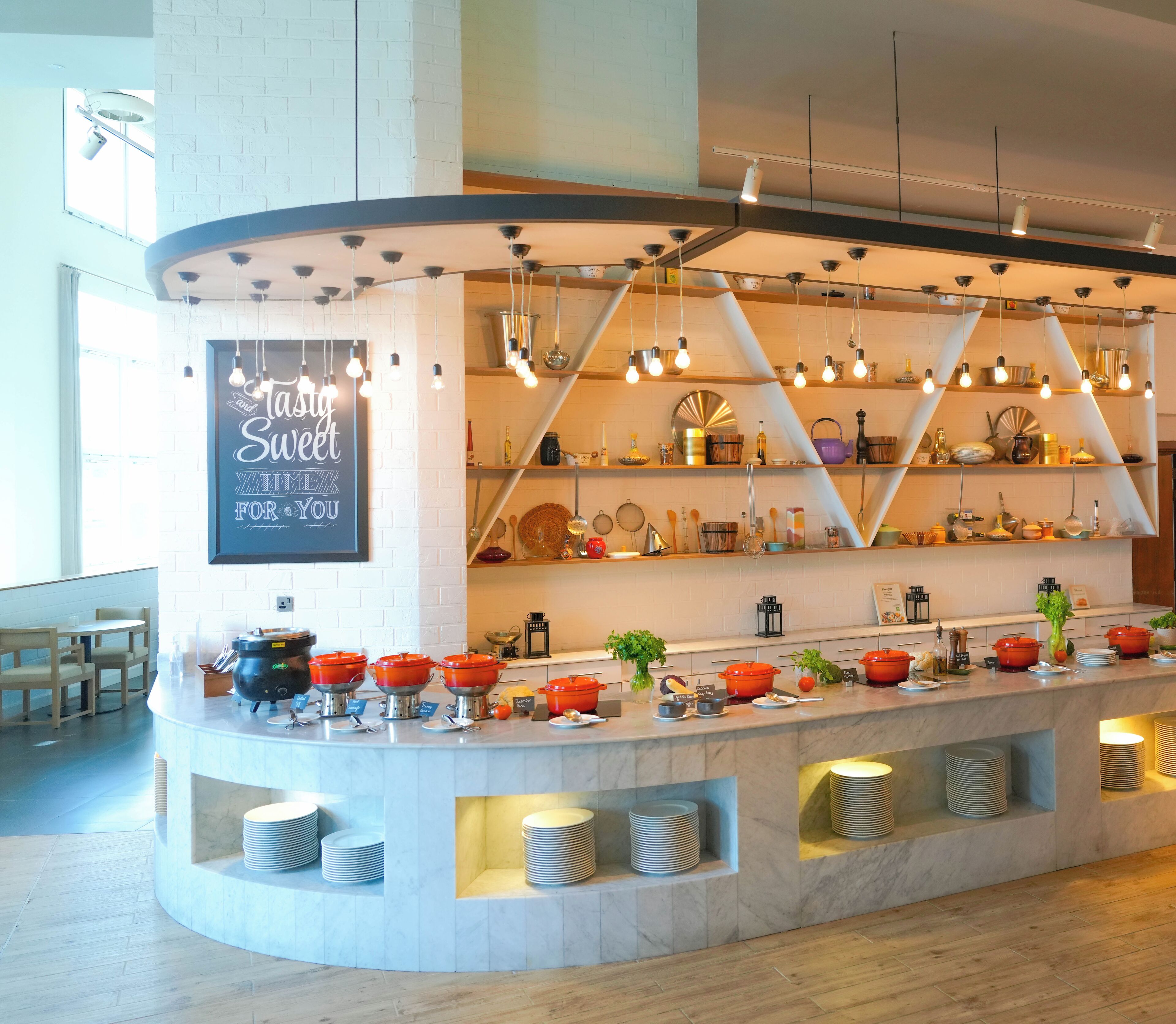 A buffet setup with a variety of dishes and utensils, a sign that reads "Stay Sweet," and a modern interior design with exposed brick walls and pendant lighting.