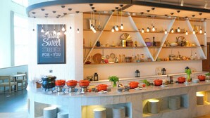 Ein reichhaltiges Buffet mit verschiedenen Speisen und Besteck, ein Schild mit der Aufschrift "Stay Sweet" sowie ein modernes Interieur mit freiliegenden Backsteinwänden und Pendelleuchten.