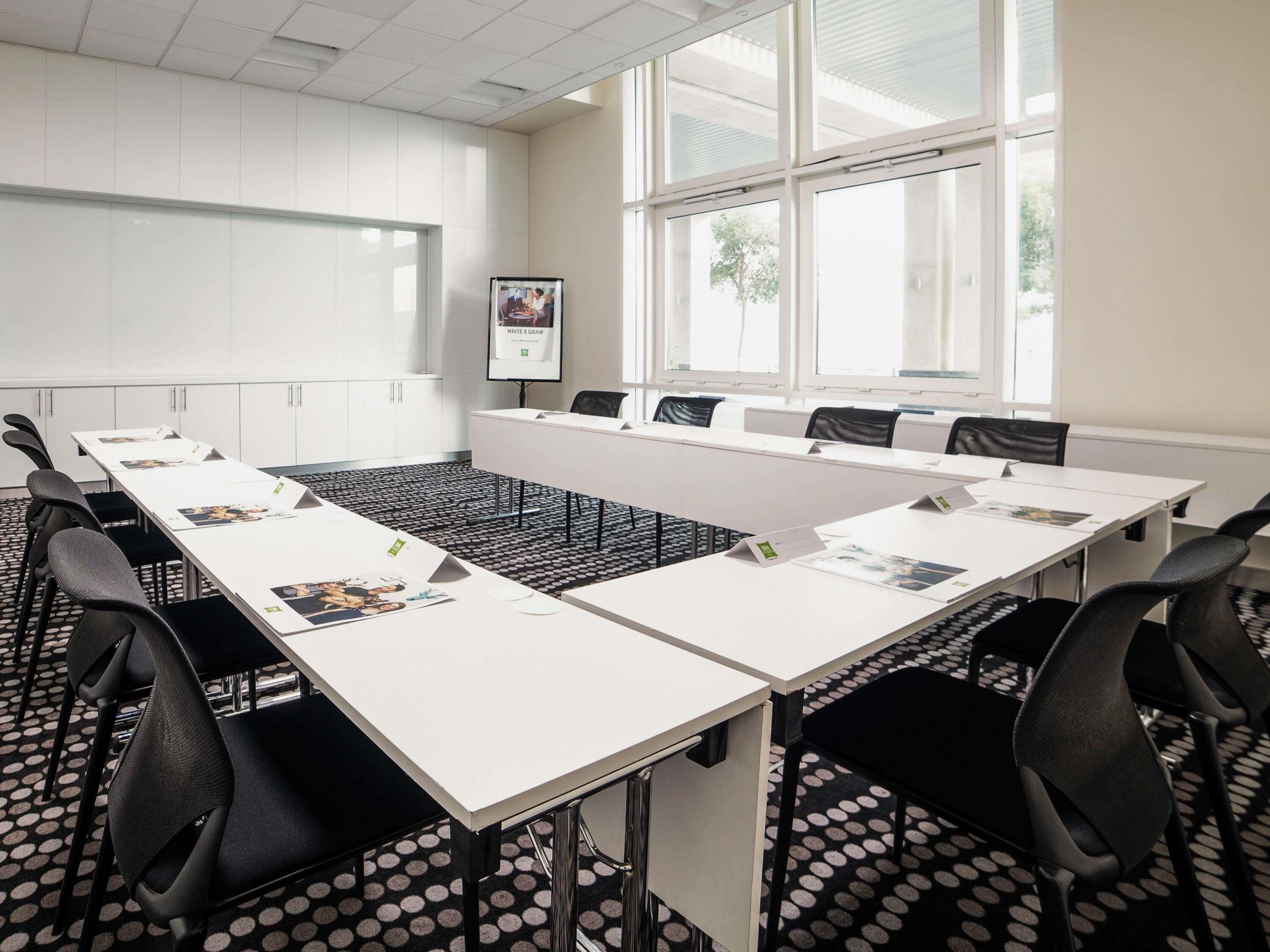 A conference room with a long table, chairs, a whiteboard, and large windows.