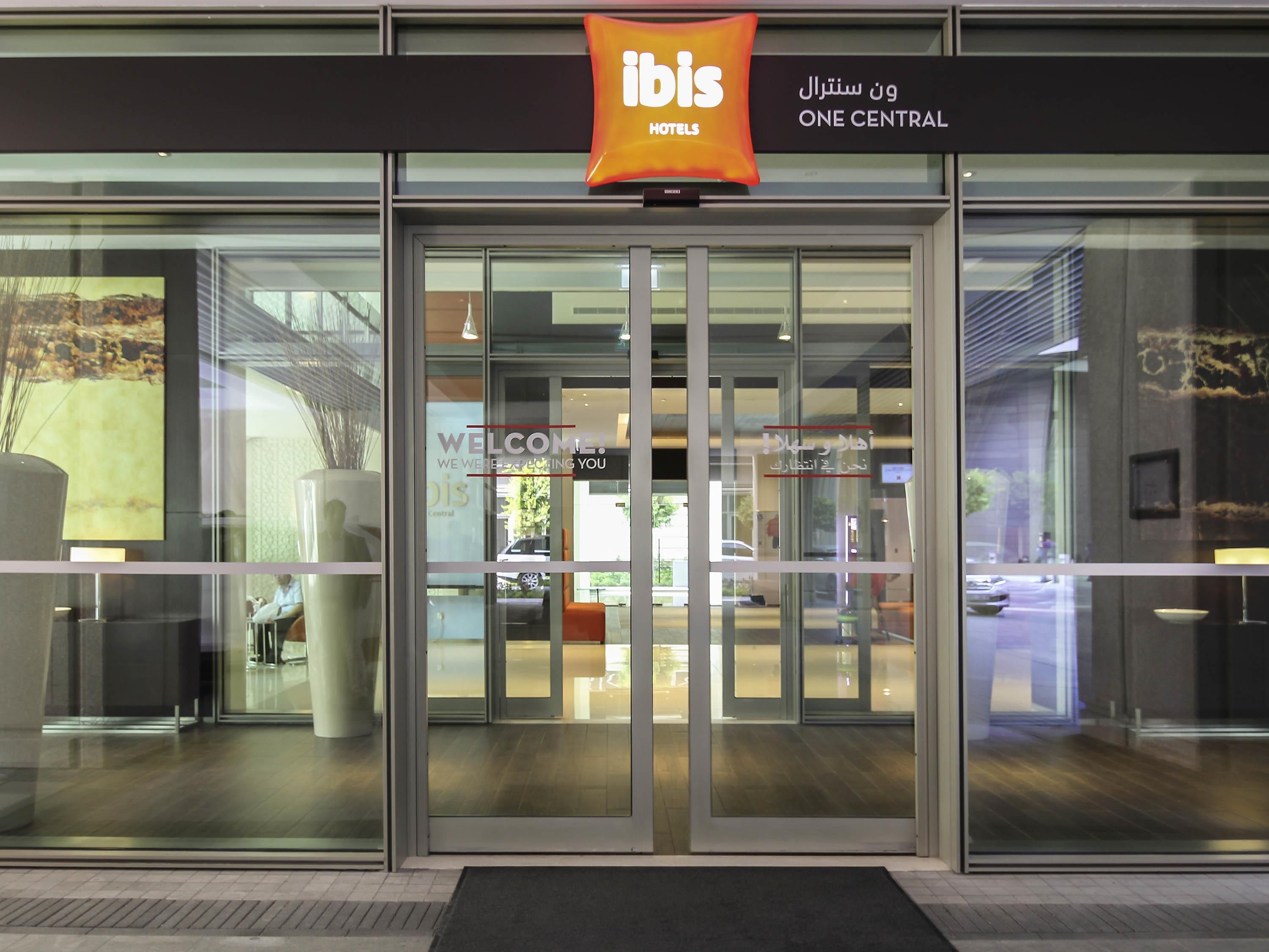 A hotel entrance with glass doors, a welcome sign, and a sign indicating 'One Central'.