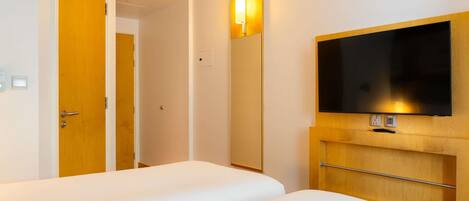 Habitación de hotel con cama, televisión instalada en un panel de madera, una puerta y una lámpara.