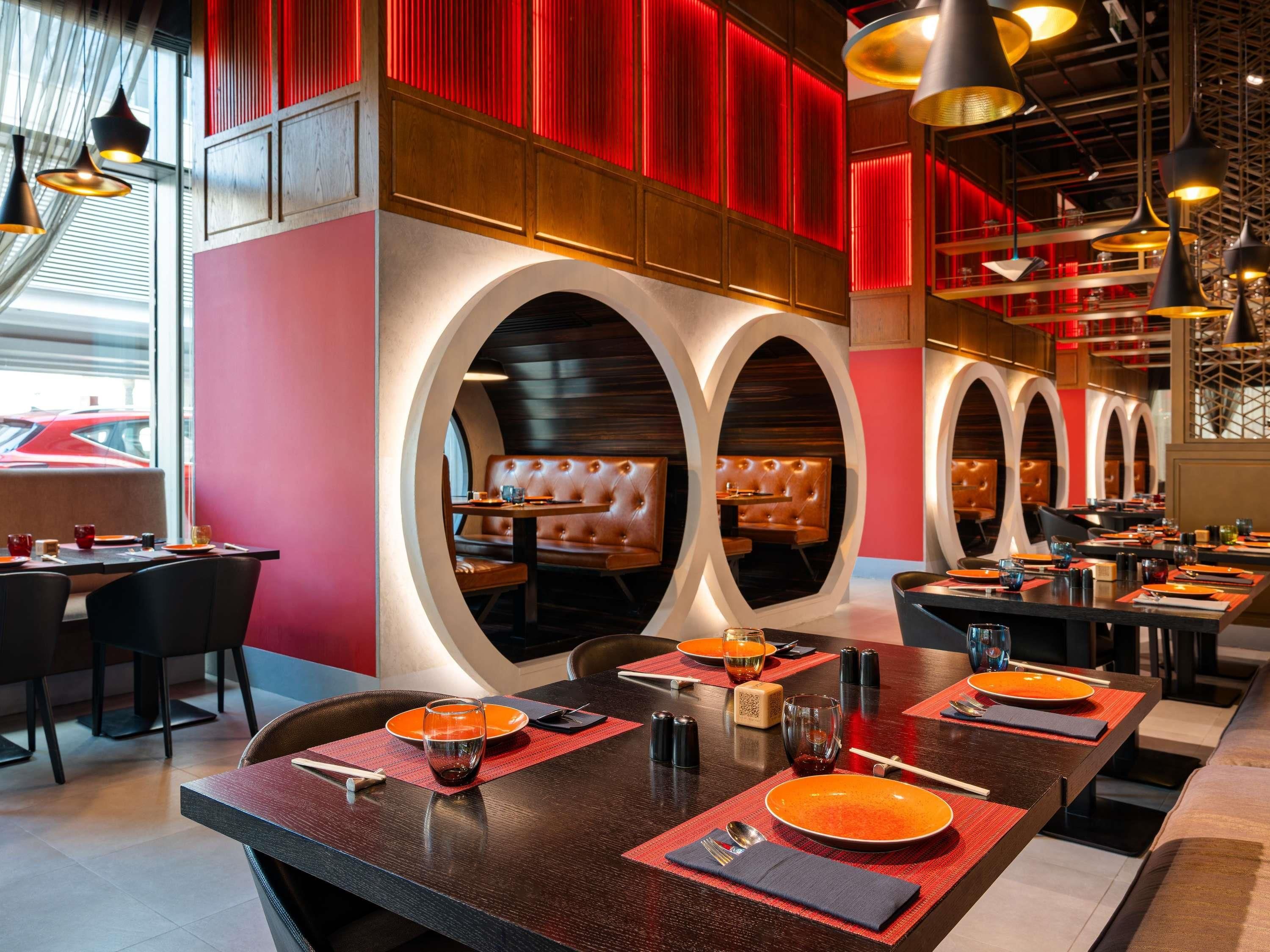 Un restaurante con mesas redondas, asientos de cuero y detalles en rojo.