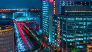 A modern hotel with a prominent 'ibis' sign, surrounded by illuminated buildings and a busy road with light trails.