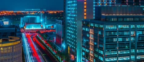 Un hotel moderno con un llamativo letrero de 'ibis', rodeado de edificios iluminados y una calle concurrida con estelas de luz.
