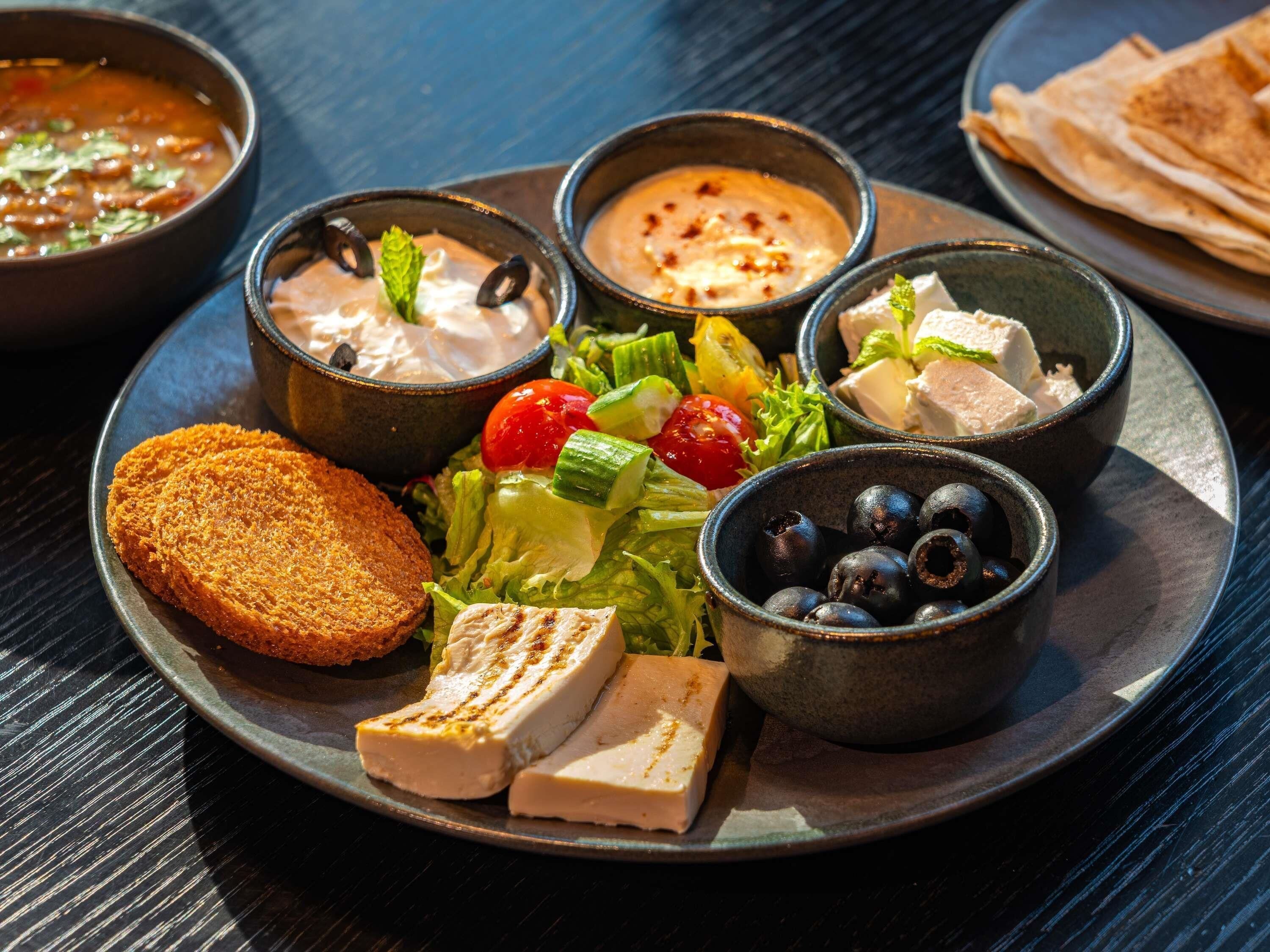 A plate with various food items including a salad, grilled chicken, bread, and bowls of dips.