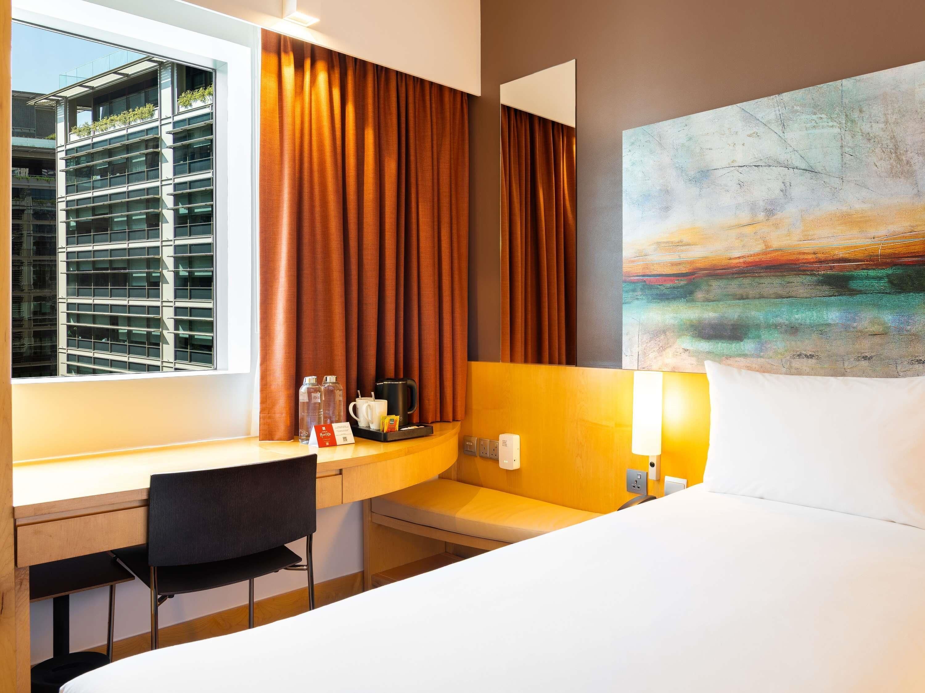 A hotel room with a desk, chair, bed, and a large window with curtains.