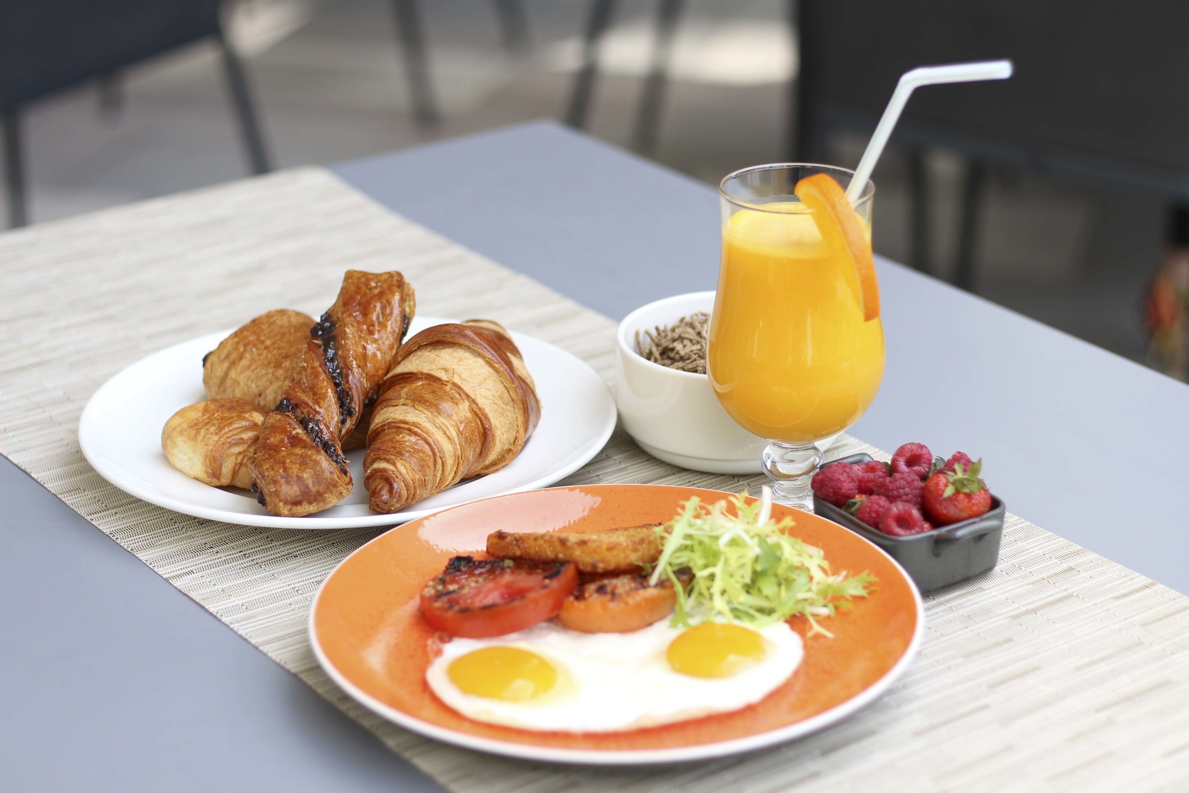 A breakfast setting with croissants, eggs, tomatoes, and a glass of orange juice on a table.