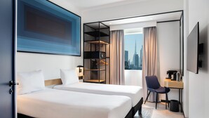 A hotel room with two beds, a desk, a chair, a TV, and a view of a cityscape.
