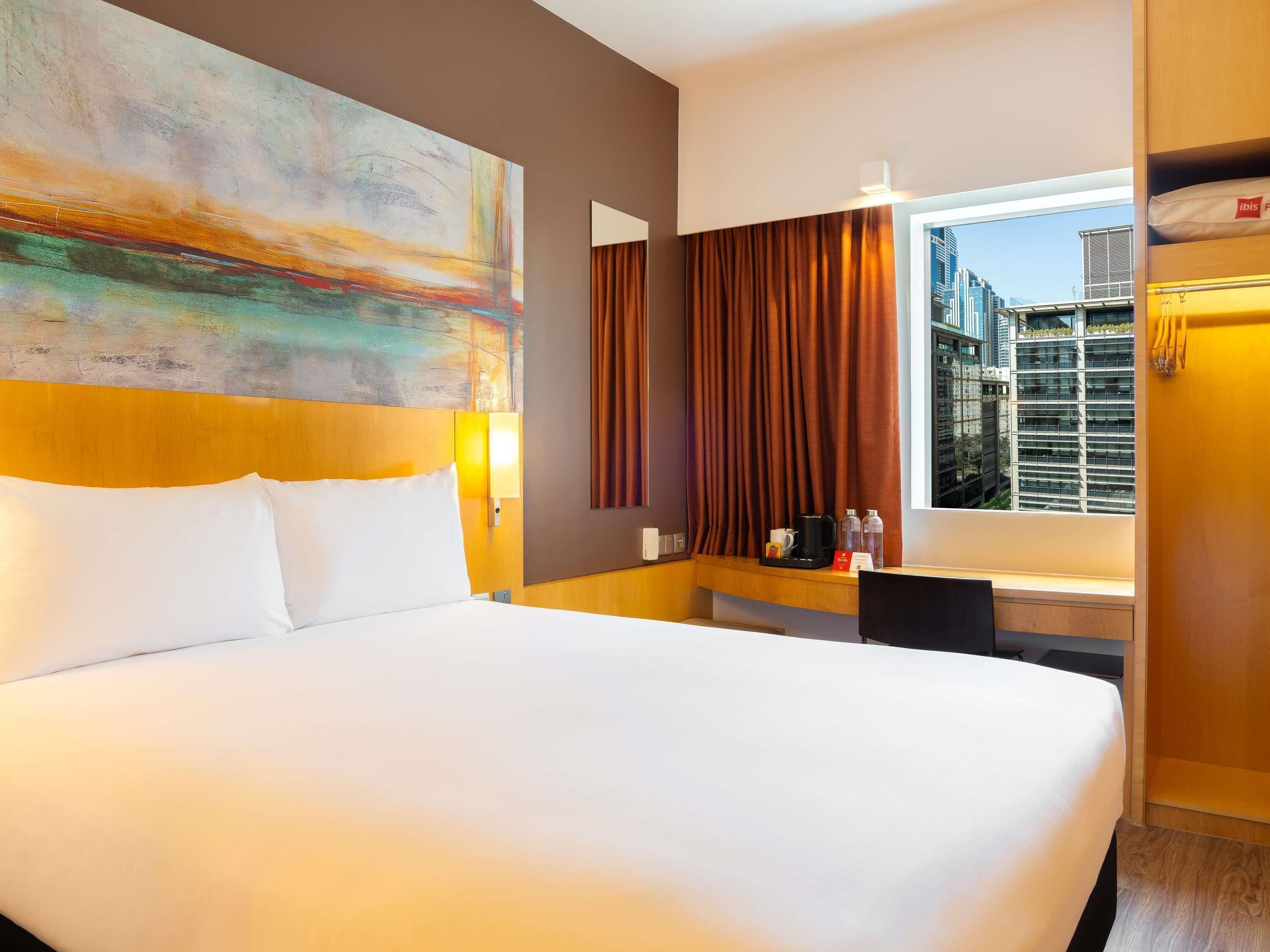 Hotellihuone, jossa on suuri sänky, työpöytä kahvinkeittimellä, ikkuna verhoilla ja näkymä kaupunkiin.