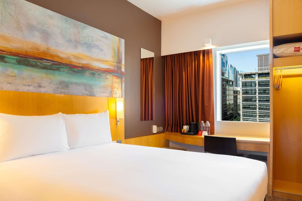 Hotellihuone, jossa on suuri sänky, työpöytä kahvinkeittimellä, ikkuna verhoilla ja näkymä kaupunkiin.