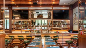 A bar with wooden decor, multiple seating areas, and a variety of bottles on shelves.