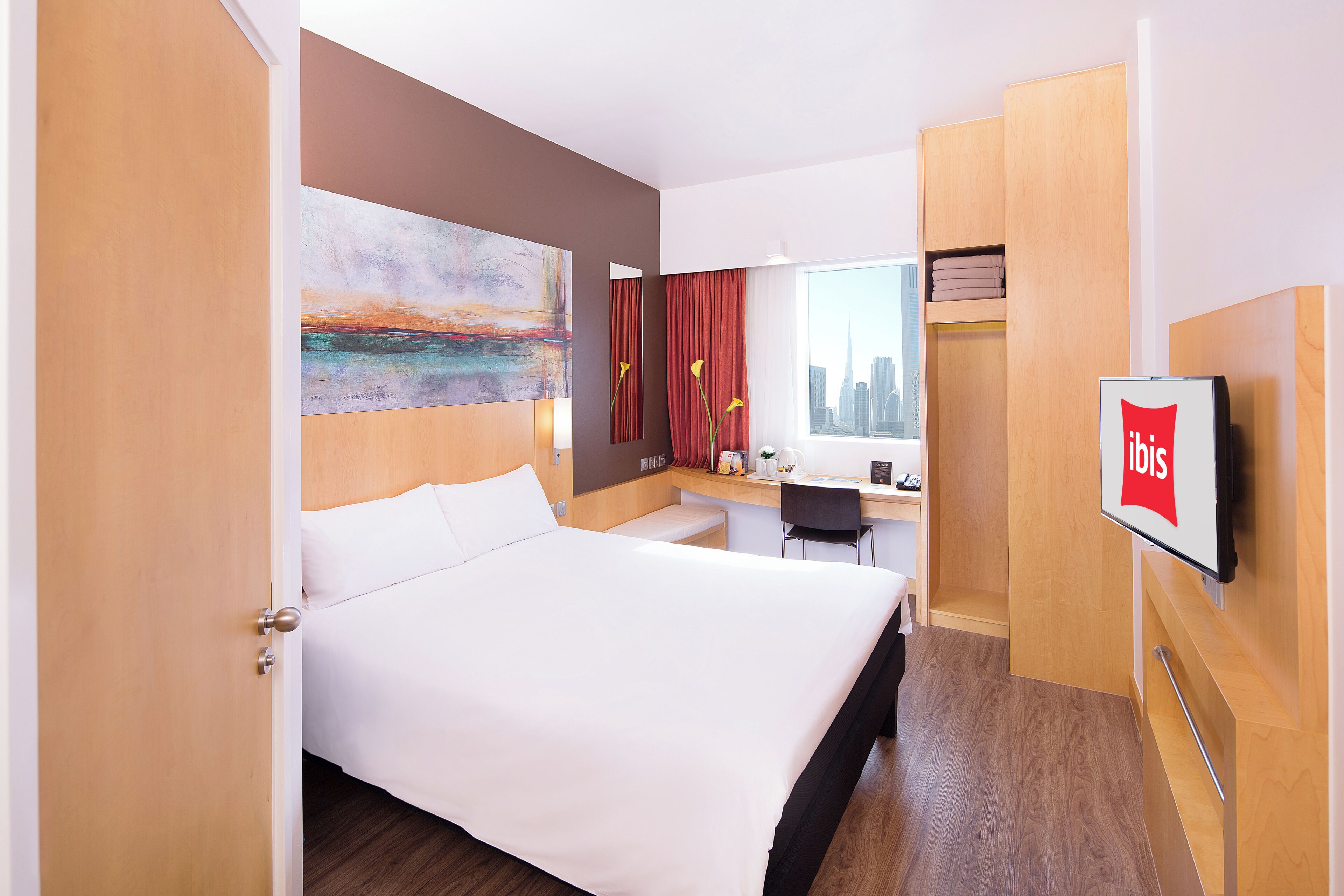 Una habitación de hotel con cama, escritorio, silla, televisión y vistas a la ciudad.