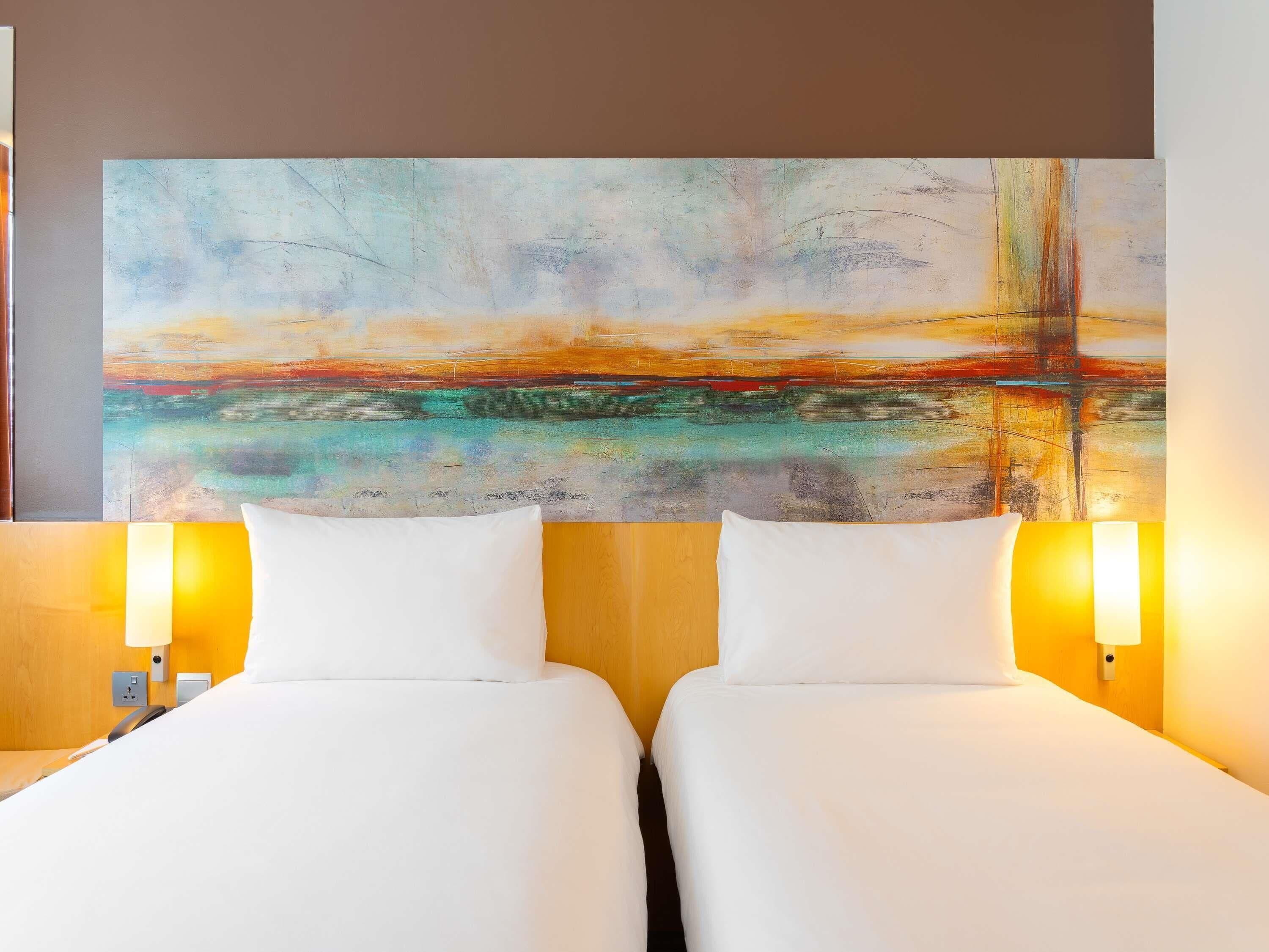 Een hotelkamer met twee bedden, een groot abstract schilderij aan de muur en twee bedlampen.