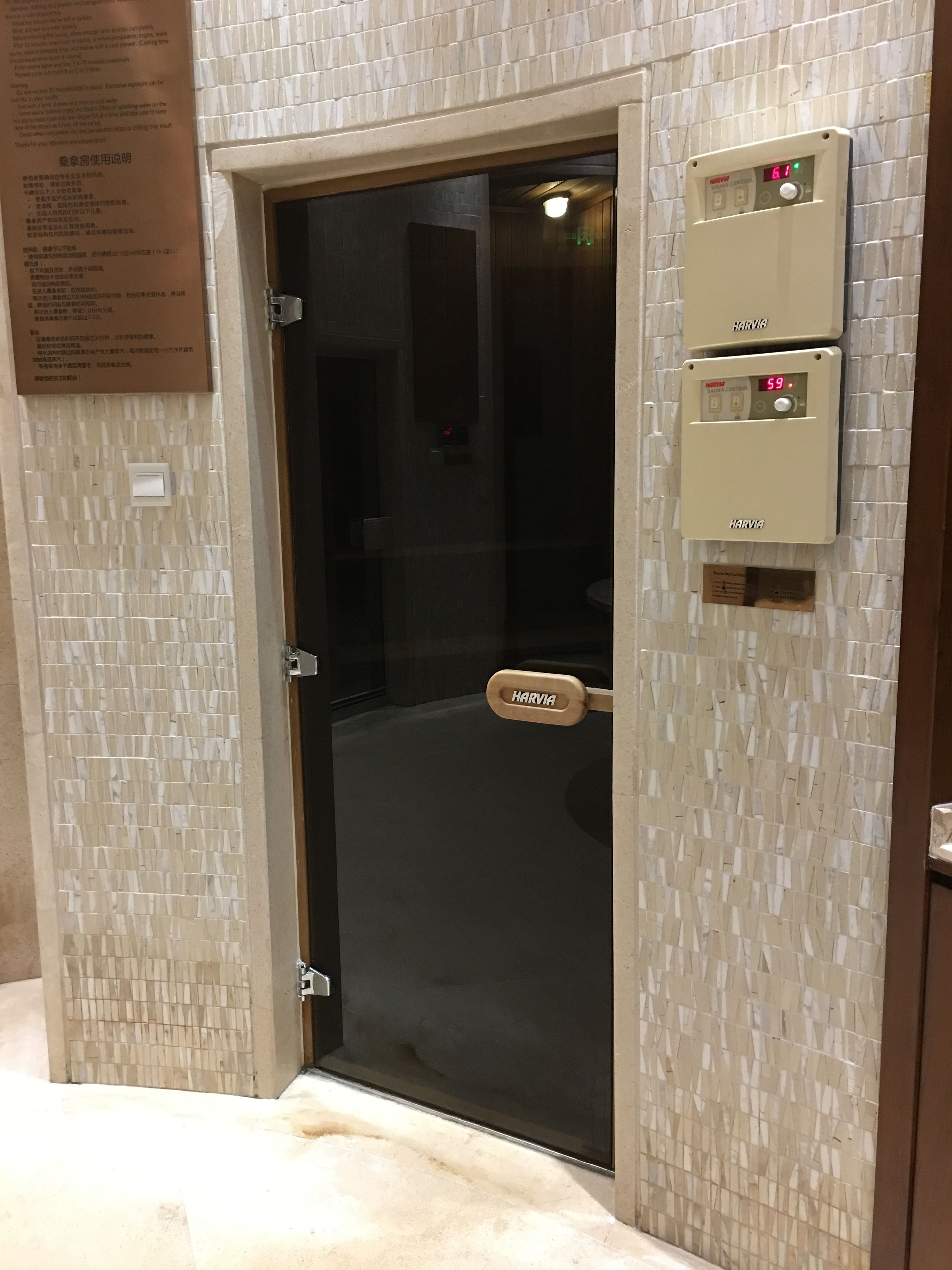 Entrada a una habitación de hotel con puerta de cristal, panel de control de sauna Harvia y el logotipo de Harvia en la puerta.