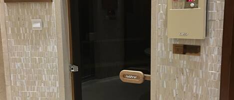 Entrada a una habitación de hotel con puerta de cristal, panel de control de sauna Harvia y el logotipo de Harvia en la puerta.