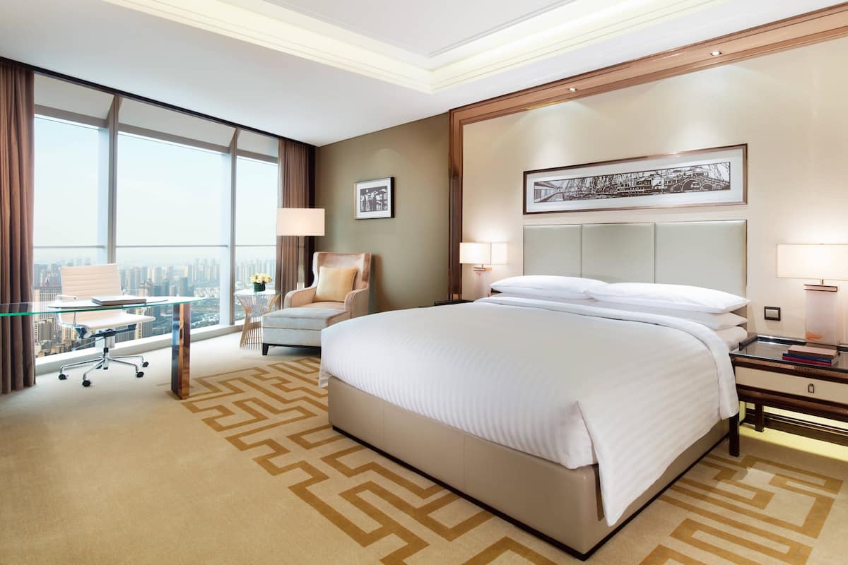 Ein Hotelzimmer mit einem großen Bett, einem Schreibtisch mit Stuhl, Blick auf die Stadt und einem großen Fenster.