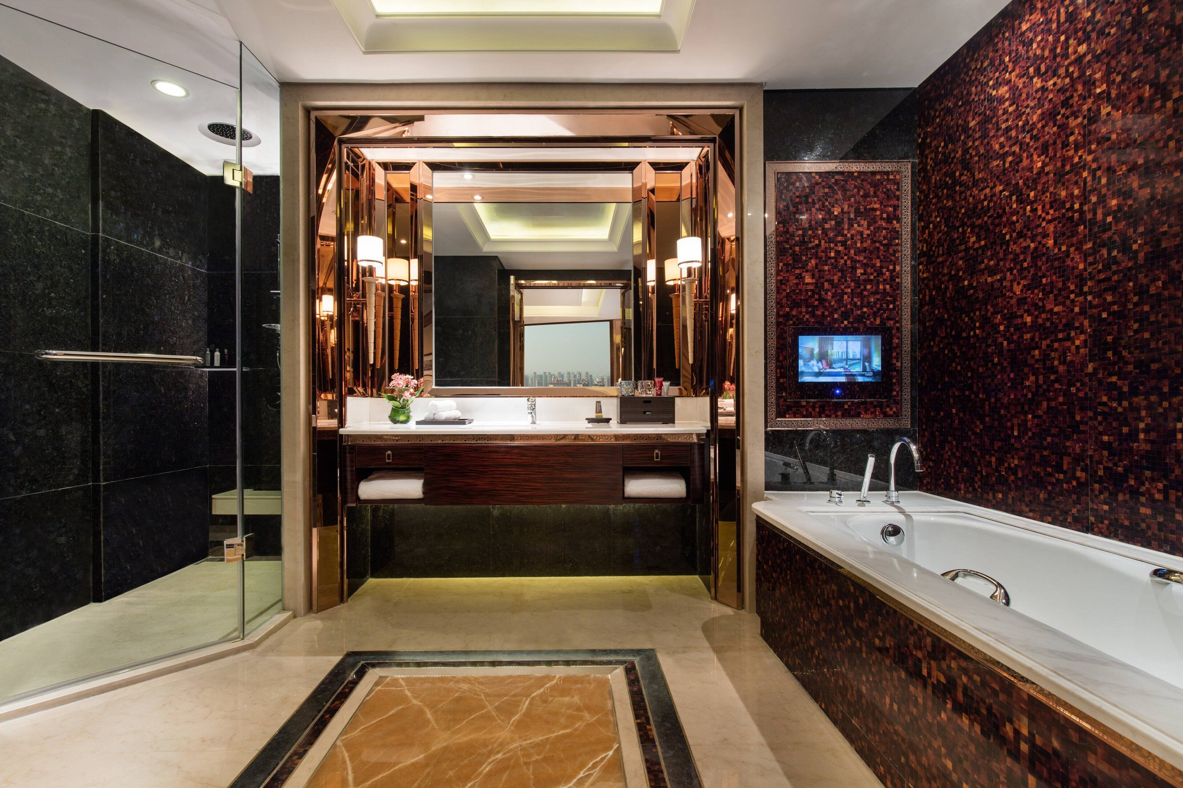 Un baño moderno con un espejo grande, lavamanos dobles, bañera y televisor en la pared.