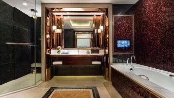 Un baño moderno con un espejo grande, lavamanos dobles, bañera y televisor en la pared.