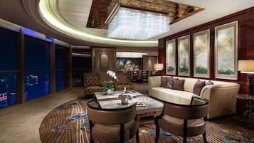 A modern hotel lobby with a round table, comfortable seating, large windows with city views, and artwork on the walls.