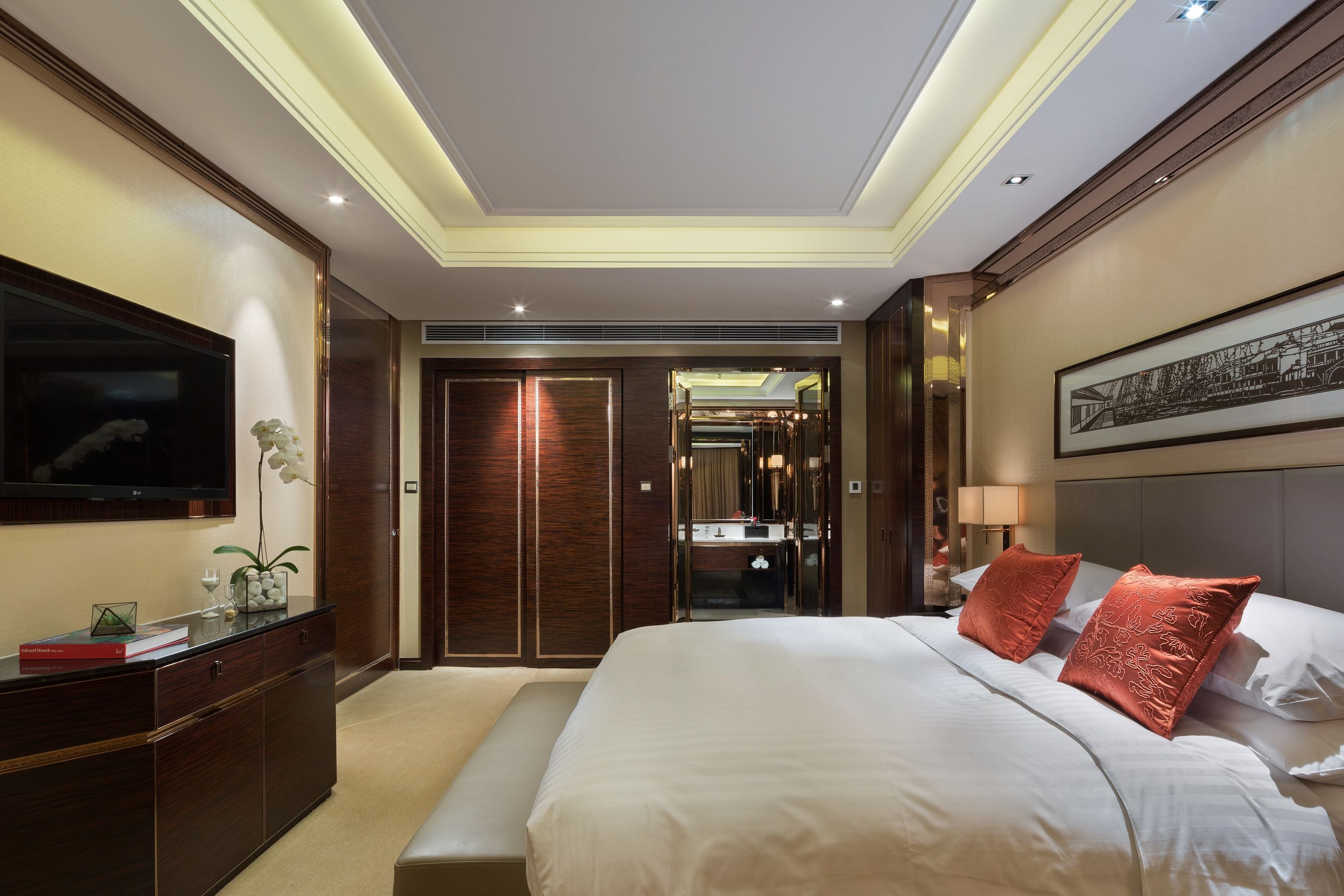 Une chambre d’hôtel avec un grand lit, un téléviseur fixé au mur, un bureau agrémenté d’une plante et un miroir.