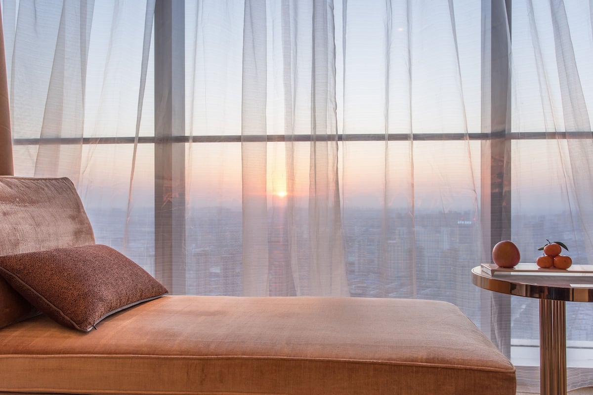 Ein modernes Zimmer mit einer Couch, einem kleinen Tisch und Blick auf die Stadt durch transparente Vorhänge.