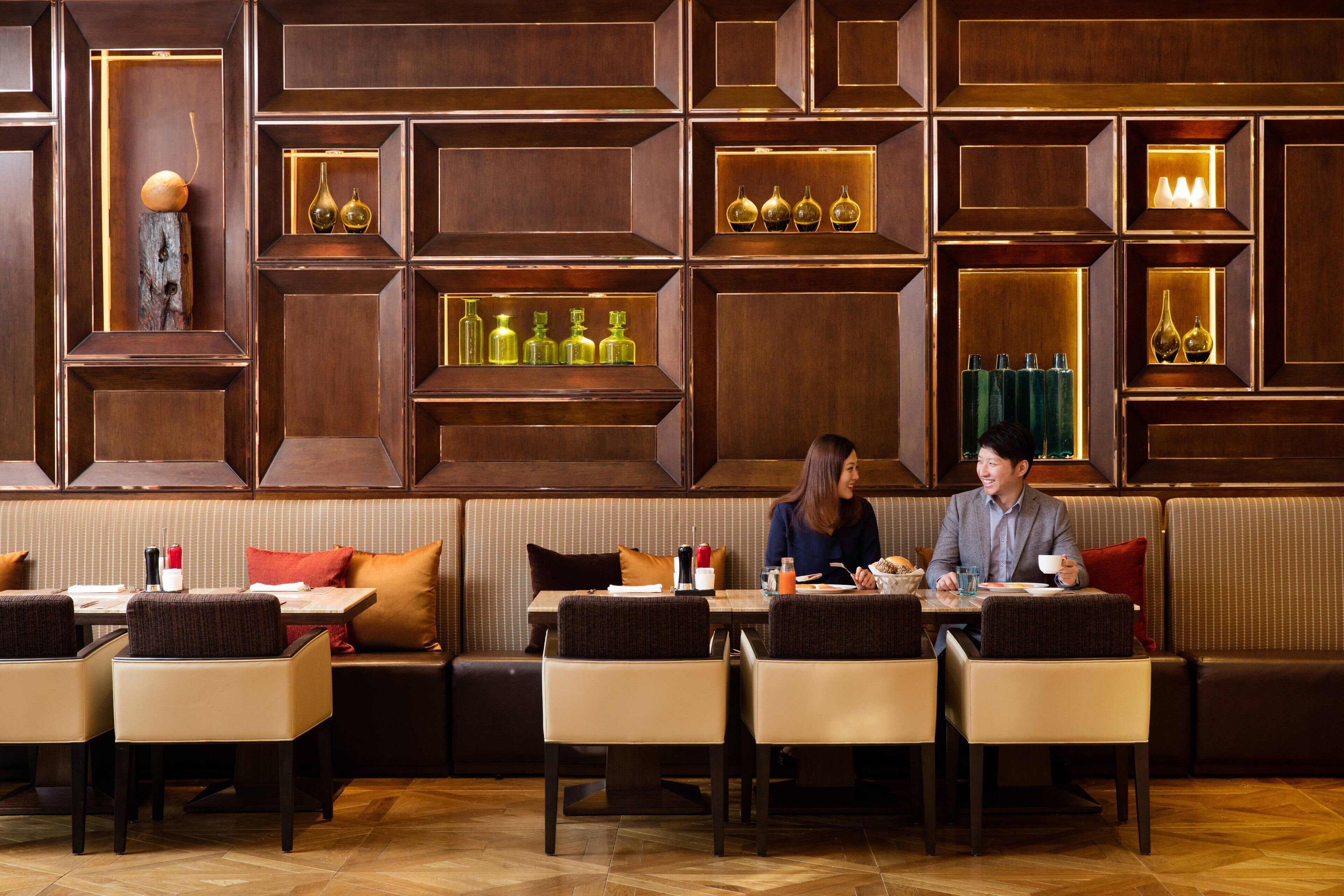Un restaurante con paneles de madera e iluminación empotrada. Varias zonas de estar con mesas y sillas.
