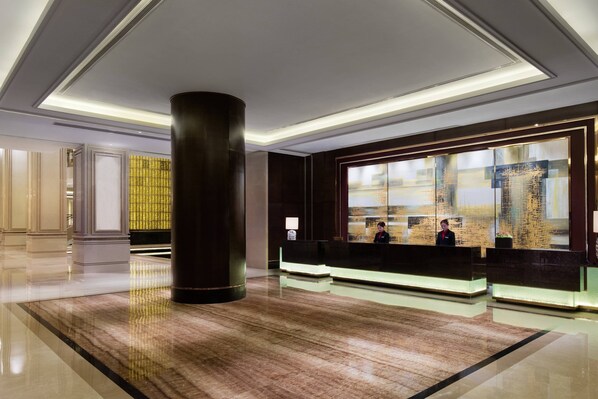 A modern hotel lobby with a large reception desk, a tall pillar, and a large window with a view of the city. - Changzhou Marriott Hotel (Changzhou)