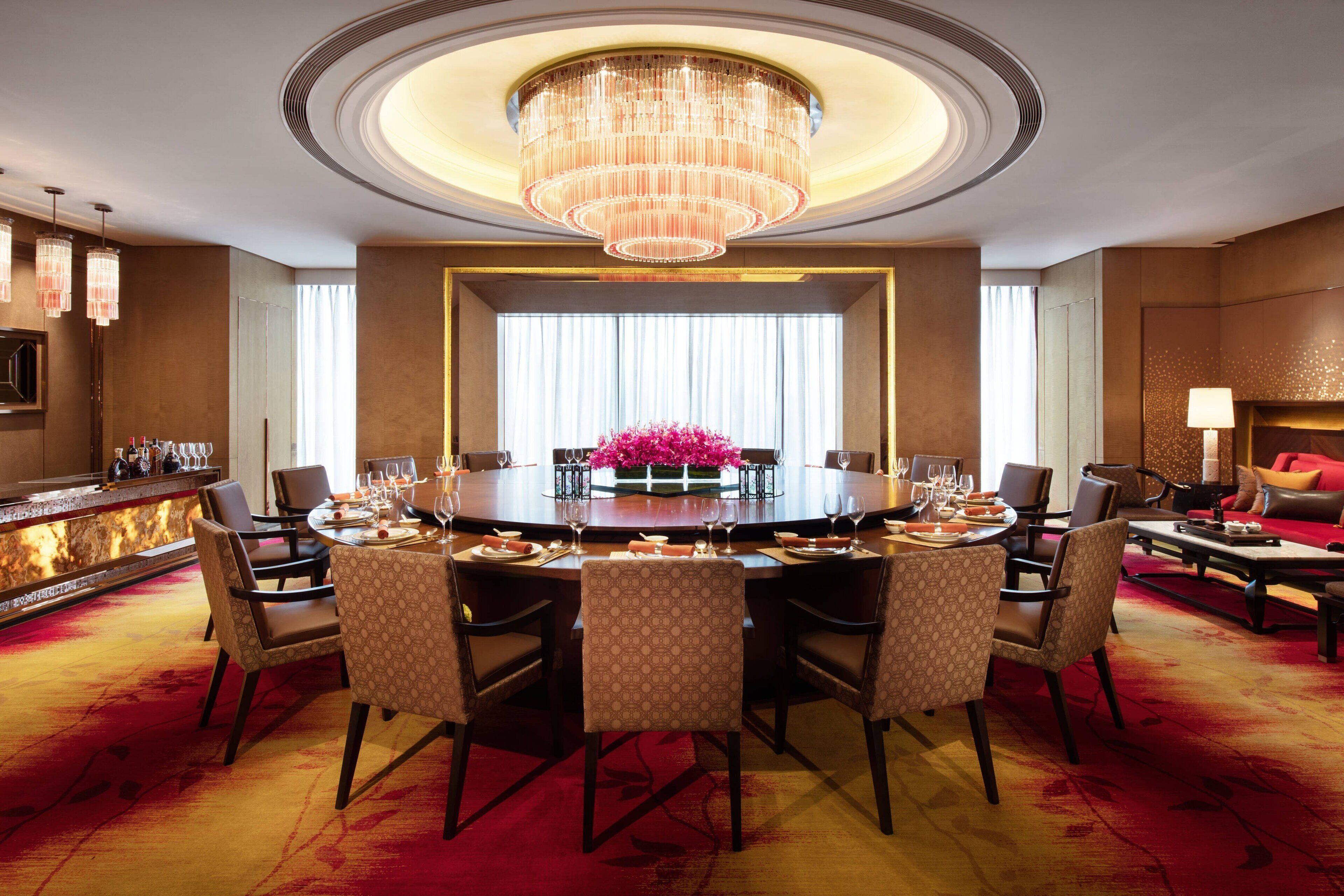 A spacious dining area with a round table, multiple chairs, a chandelier, and a bar counter.