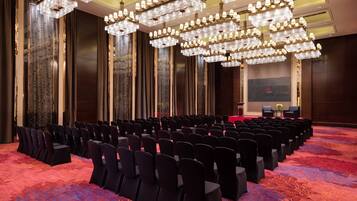A conference room with rows of chairs, a stage, and a large chandelier.