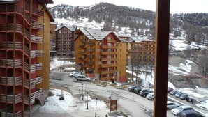 Ein Hotel mit mehreren Etagen und Balkonen, gelegen in einer verschneiten Berglandschaft mit Parkplatz vor dem Haus.