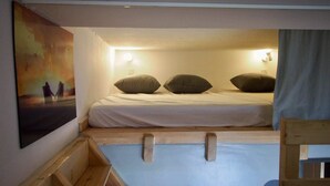 Ein kleiner, gemütlicher Raum mit einem Etagenbett, einer Holzleiter und einem Einzelbett.