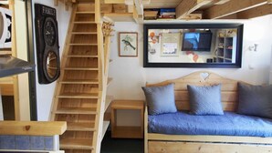 Ein gemütlicher Raum mit einer Holztreppe, einem Sofa mit Kissen, einer Wanduhr und einem Fernseher über einem Spiegel.