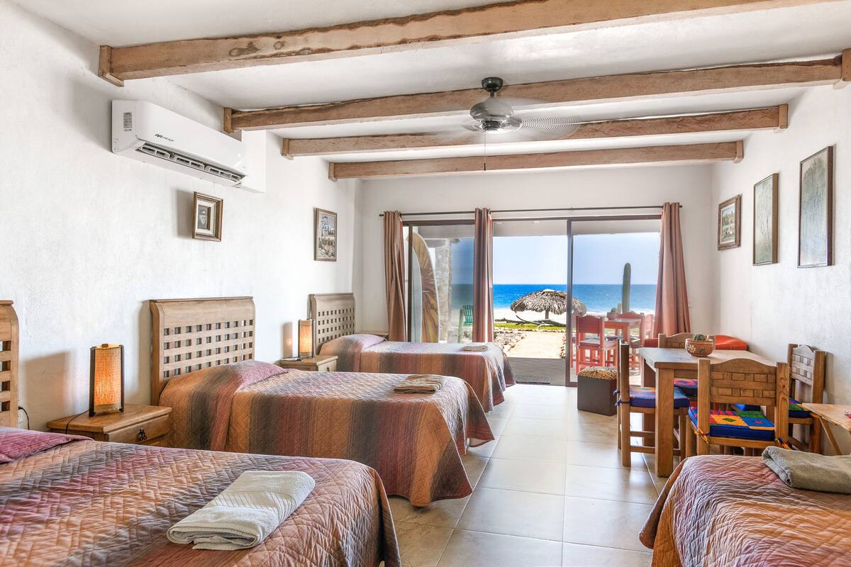 A hotel room with three beds, a dining table, and a view of the beach.