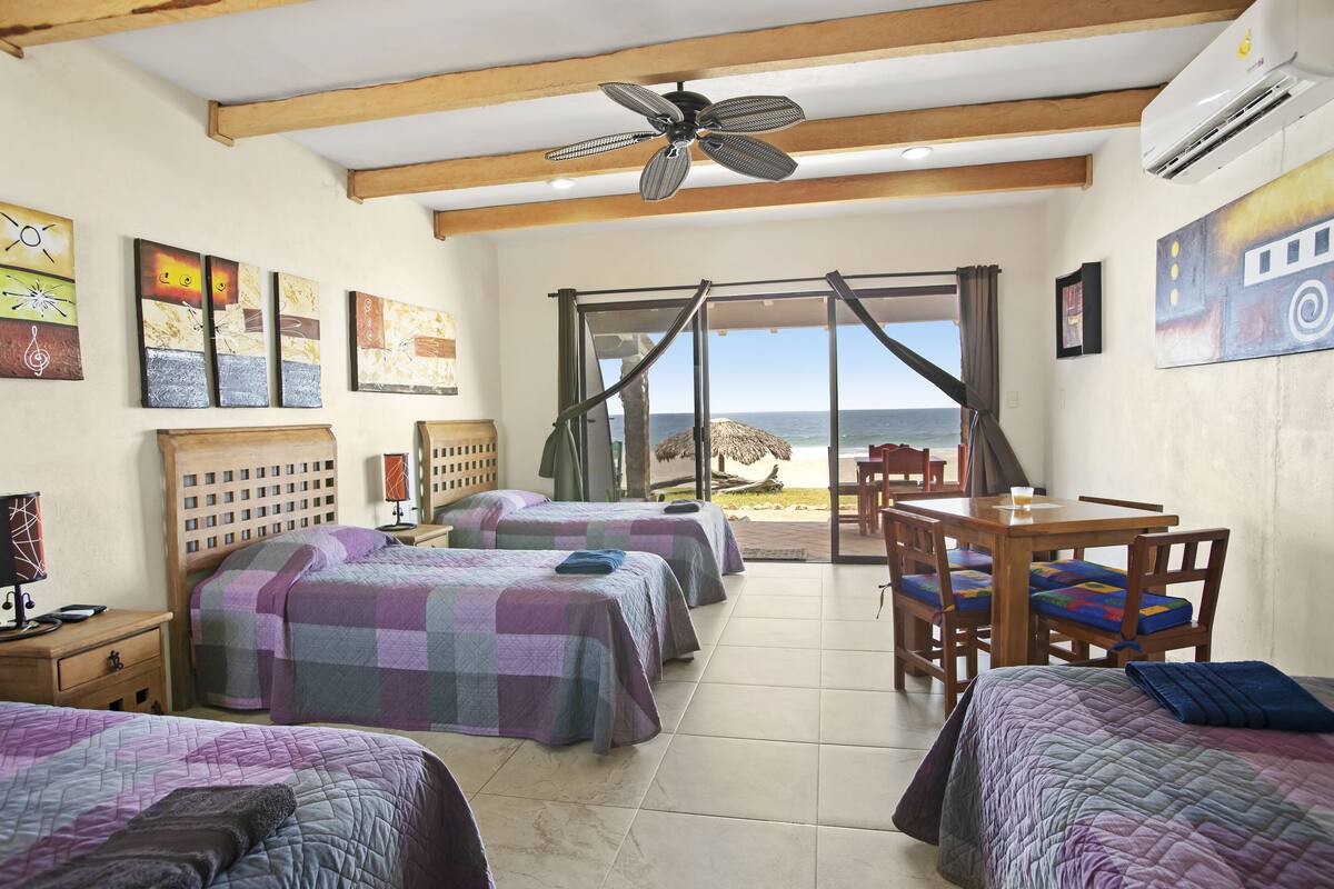 A hotel room with two beds, a dining table, and a view of the beach.