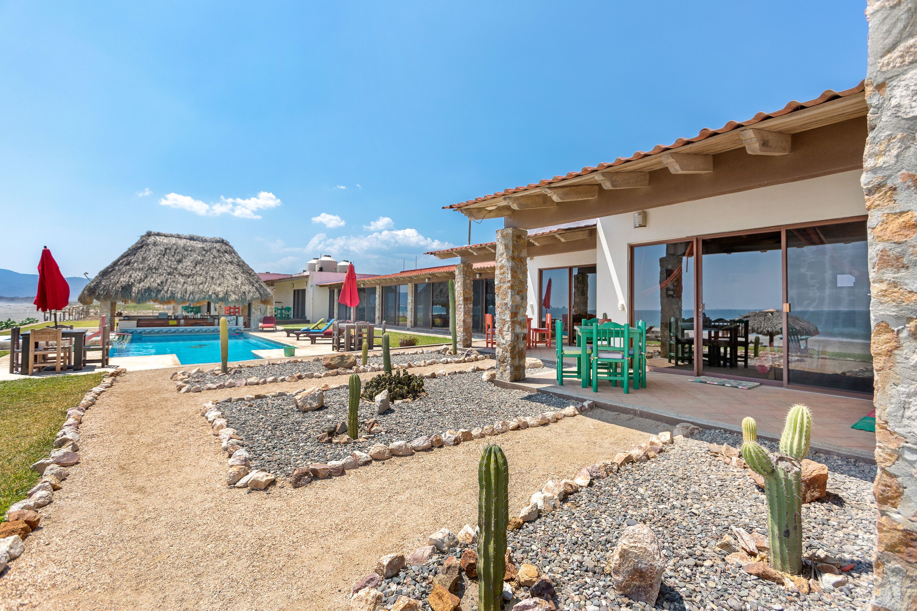 A pool area with a thatched roof structure, outdoor seating, and a cactus garden.