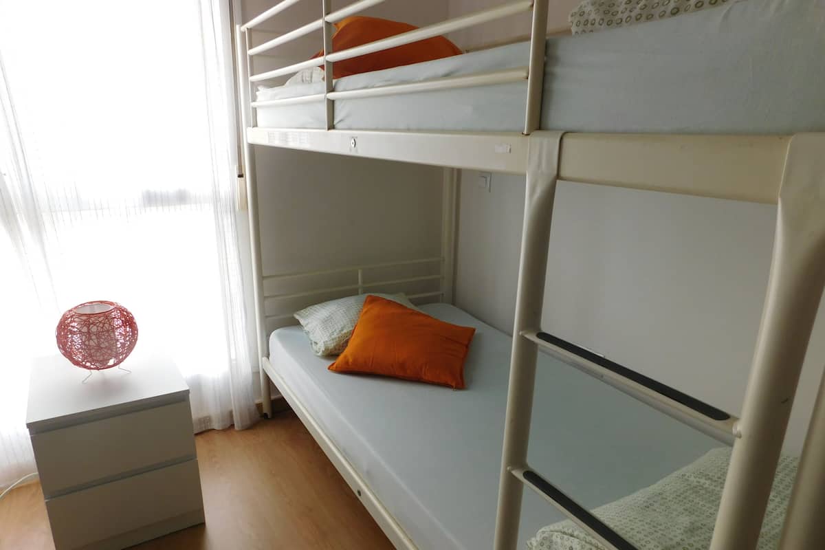 Quarto com beliche, cômoda branca e um objeto esférico vermelho sobre uma mesa.