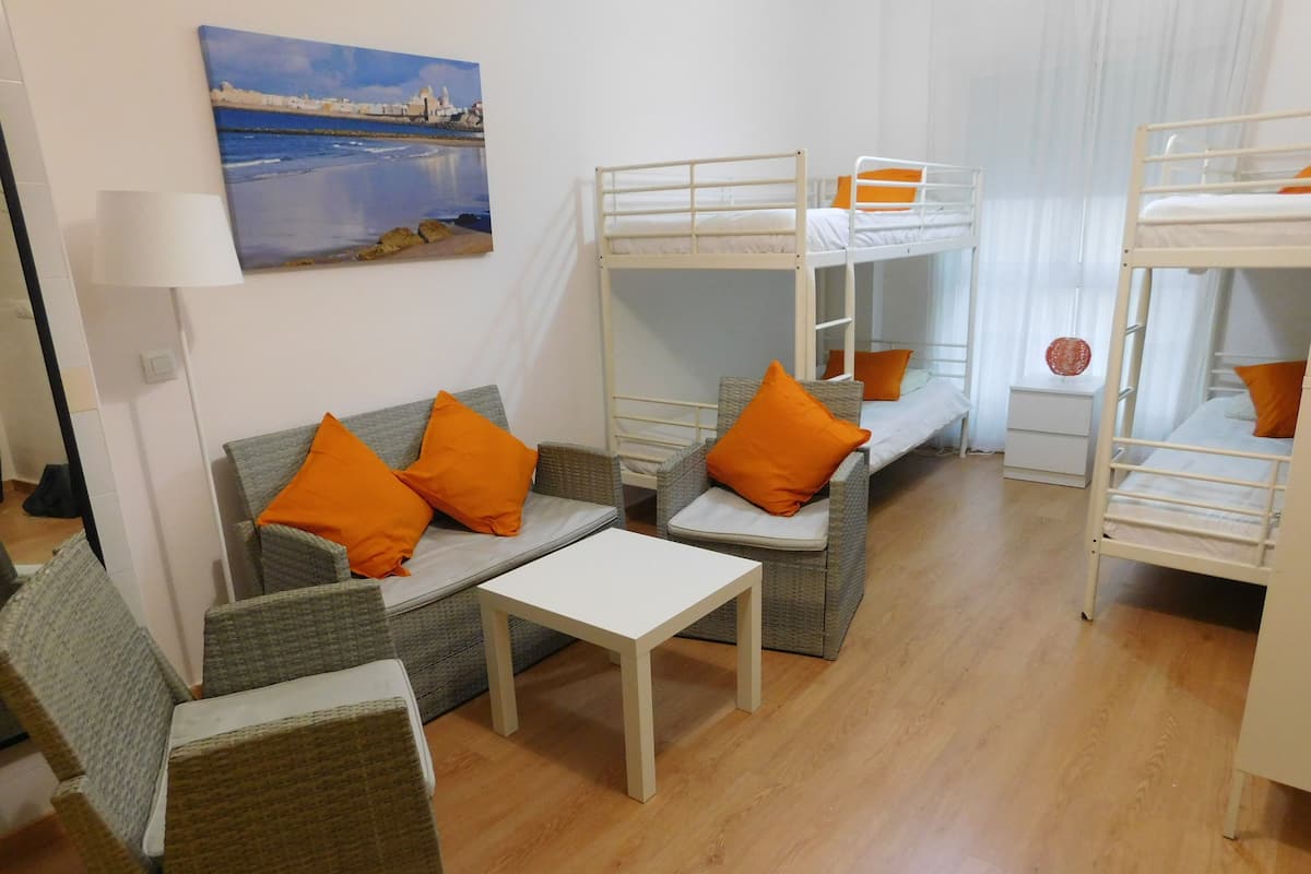 Quarto com sofá, duas poltronas, uma mesinha e beliches.