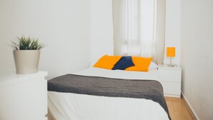 A bedroom with a bed, a nightstand with a lamp, a potted plant, and a window with sheer curtains. - Cádiz INN Hostel (Cádiz)