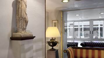 Una estatua sobre un pedestal, una lámpara en una mesa y un sofá en una habitación con ventana y luces en el techo.