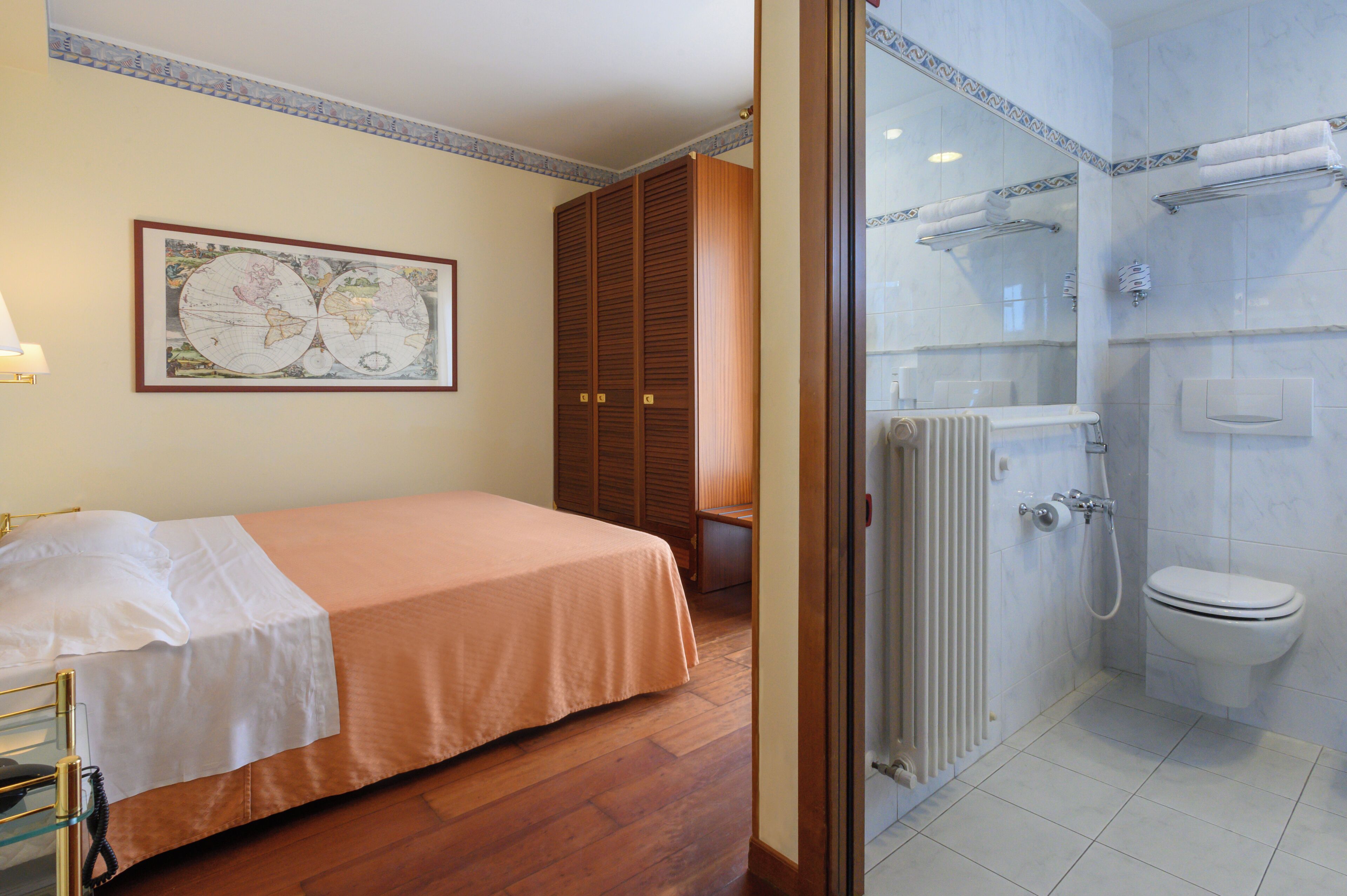Une chambre d’hôtel avec un lit, une carte accrochée au mur, une armoire, une salle de bain avec des toilettes et une douche.