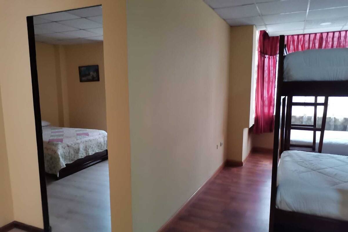 Quarto com beliche, uma cama de solteiro, uma mesa pequena e um quadro na parede.